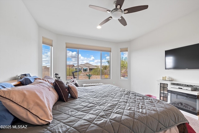 bedroom with a glass covered fireplace, carpet flooring, and ceiling fan