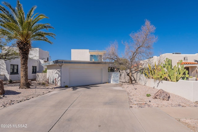 view of front of home featuring stucco siding, a garage, driveway, and fence