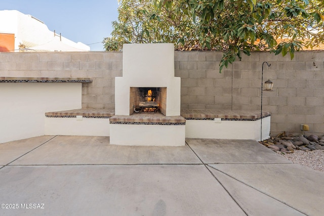view of patio featuring a lit fireplace and fence