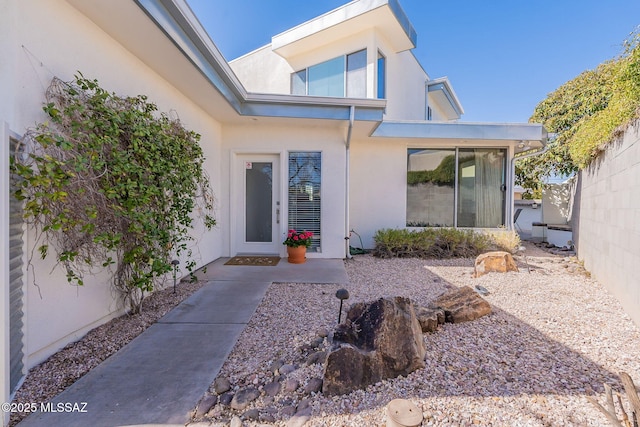 view of exterior entry featuring stucco siding and fence