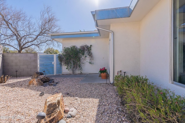 view of side of property featuring stucco siding, a patio area, and fence