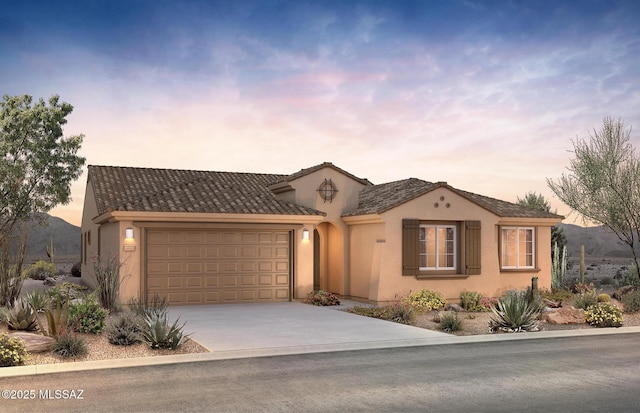 mediterranean / spanish house featuring stucco siding, a garage, driveway, and a tiled roof