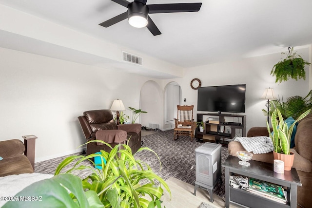 carpeted living room with visible vents, arched walkways, baseboards, and a ceiling fan