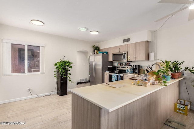 kitchen featuring visible vents, a peninsula, arched walkways, stainless steel appliances, and light countertops