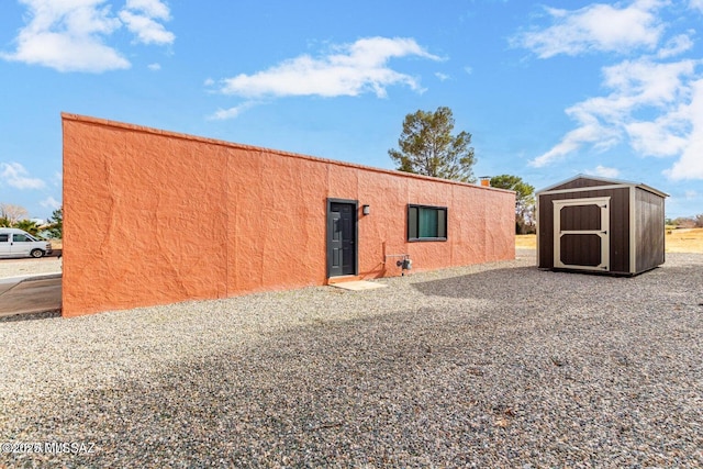 rear view of property featuring stucco siding, a storage shed, and an outdoor structure