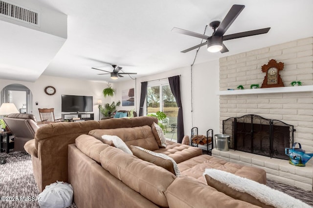 living room featuring a brick fireplace, arched walkways, visible vents, and ceiling fan