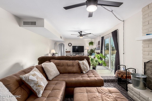 living area featuring arched walkways, a fireplace, visible vents, and ceiling fan