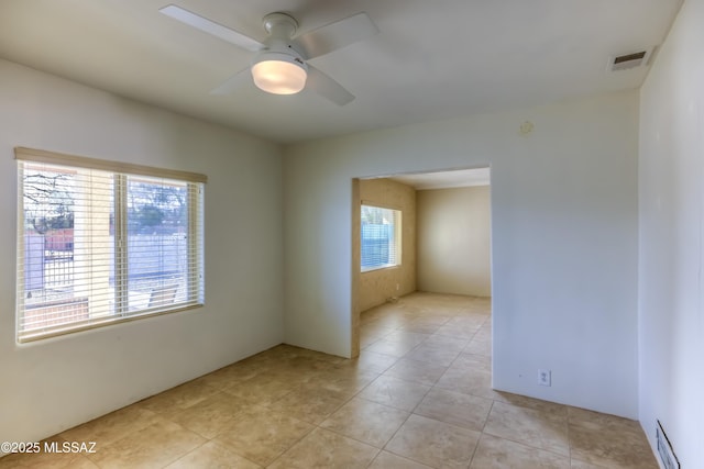 unfurnished room with plenty of natural light, a ceiling fan, visible vents, and light tile patterned flooring