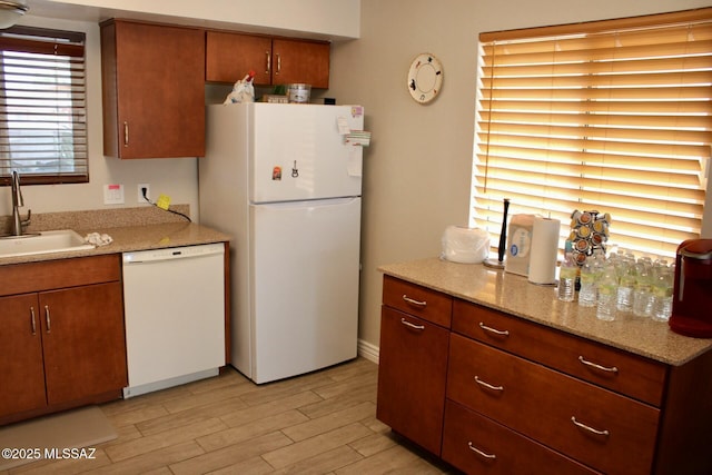 kitchen with white appliances, light stone countertops, light wood-style flooring, a sink, and brown cabinets