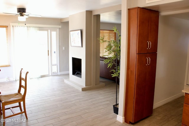 dining space featuring a ceiling fan, a fireplace with raised hearth, light wood-style floors, and baseboards