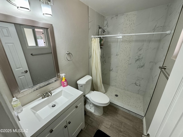 bathroom featuring a marble finish shower, wood finish floors, toilet, a textured wall, and vanity