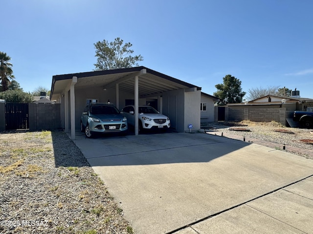 exterior space featuring an attached carport, concrete driveway, and fence