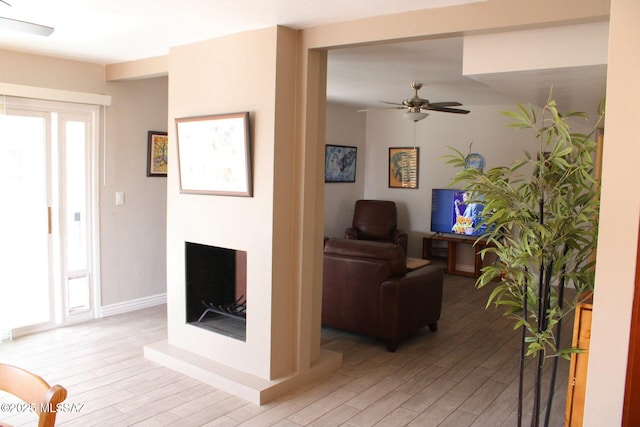 living area with a fireplace with raised hearth, light wood-style flooring, baseboards, and a ceiling fan