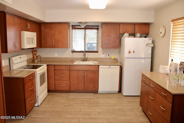 kitchen featuring brown cabinets, a sink, white appliances, light wood finished floors, and light stone countertops