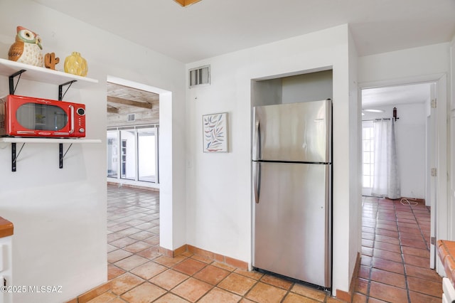 kitchen featuring freestanding refrigerator, light tile patterned floors, open shelves, and visible vents