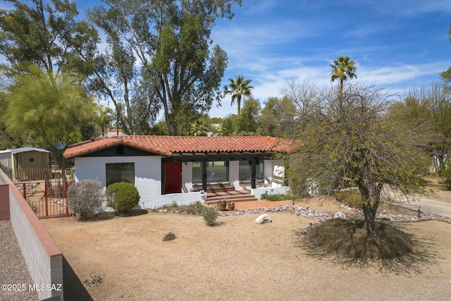 view of front of house with fence, stucco siding, covered porch, and a tiled roof