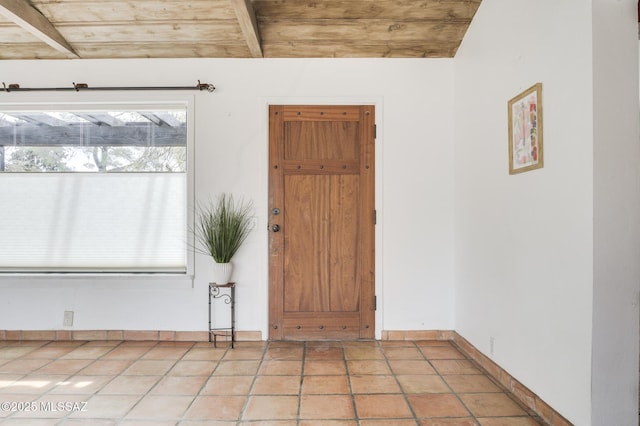 foyer entrance with light tile patterned floors, baseboards, and beamed ceiling