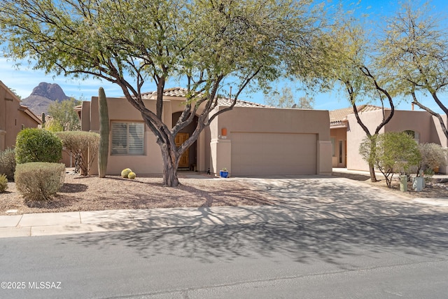 pueblo-style home with stucco siding, driveway, a tile roof, a mountain view, and an attached garage