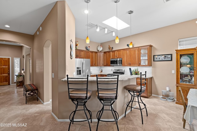 kitchen with a peninsula, a skylight, arched walkways, stainless steel appliances, and backsplash