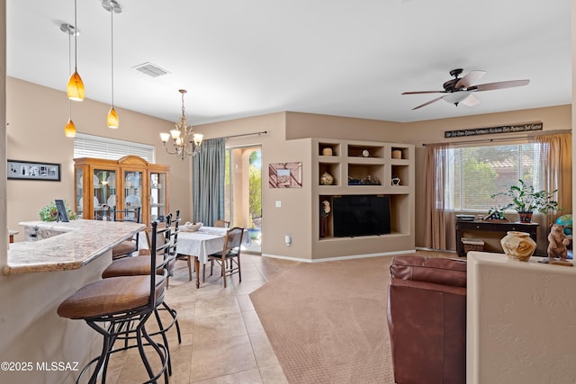 living area featuring visible vents, built in shelves, ceiling fan with notable chandelier, light tile patterned flooring, and baseboards