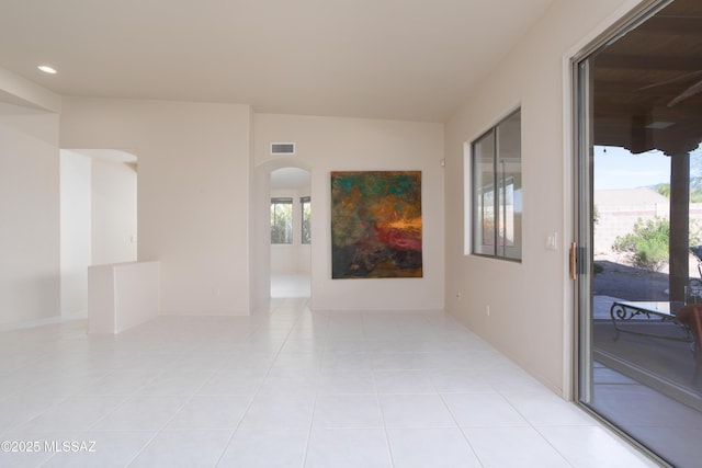 empty room with arched walkways, plenty of natural light, visible vents, and light tile patterned floors