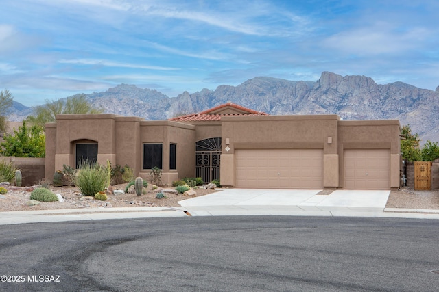 southwest-style home featuring stucco siding, driveway, a tile roof, a mountain view, and a garage