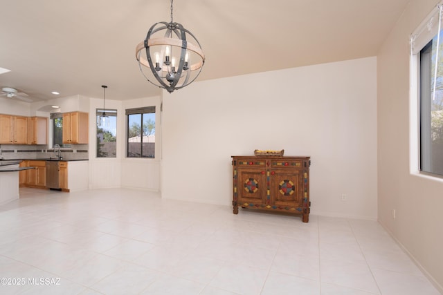 unfurnished dining area with light tile patterned flooring, ceiling fan with notable chandelier, baseboards, and a sink