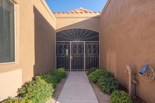 entrance to property with a tiled roof, a gate, and stucco siding