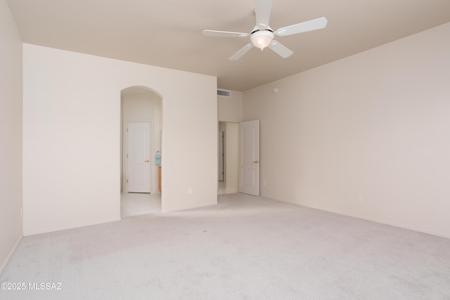 unfurnished room with visible vents, light carpet, arched walkways, baseboards, and ceiling fan