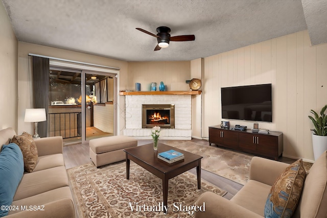 living room featuring a brick fireplace, a textured ceiling, ceiling fan, and wood finished floors