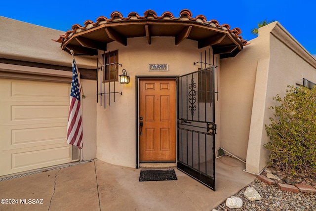 entrance to property featuring a tiled roof, an attached garage, and stucco siding