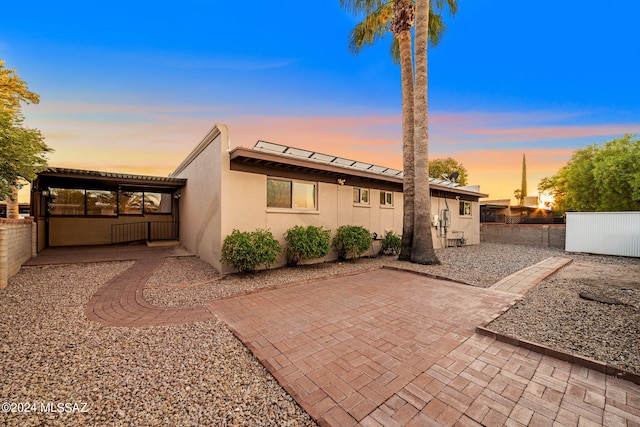 back of property at dusk with a patio area, fence, and stucco siding