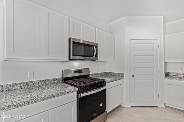 kitchen with white cabinets, light stone counters, light tile patterned floors, and stainless steel appliances