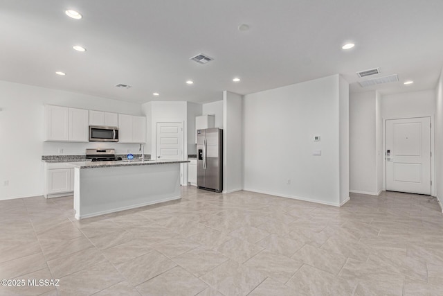 kitchen featuring visible vents, an island with sink, white cabinetry, stainless steel appliances, and light stone countertops