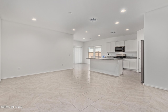 kitchen with visible vents, an island with sink, appliances with stainless steel finishes, white cabinetry, and open floor plan