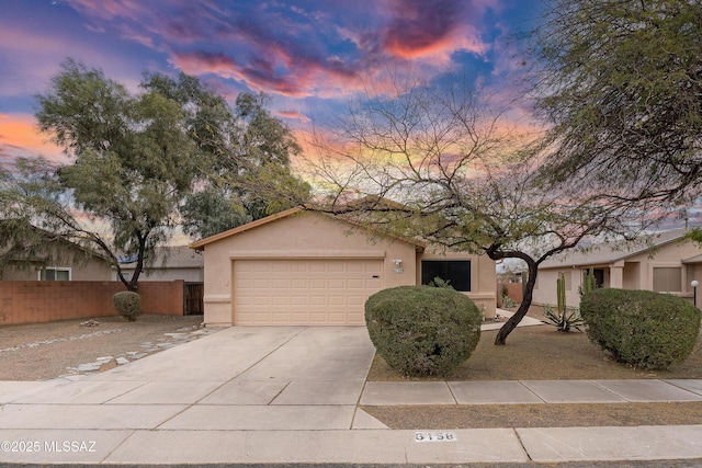 view of front of property featuring stucco siding, concrete driveway, a garage, and fence