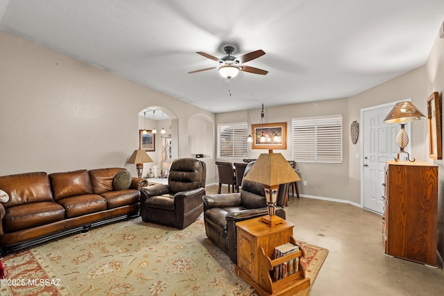 living area with arched walkways, ceiling fan, concrete flooring, and baseboards