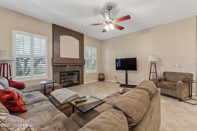 living room with a tiled fireplace, light tile patterned floors, a ceiling fan, and baseboards