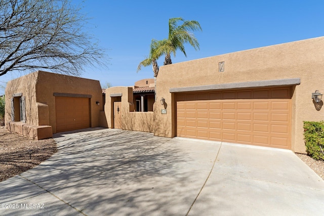 pueblo revival-style home featuring a garage, concrete driveway, stucco siding, and a tiled roof