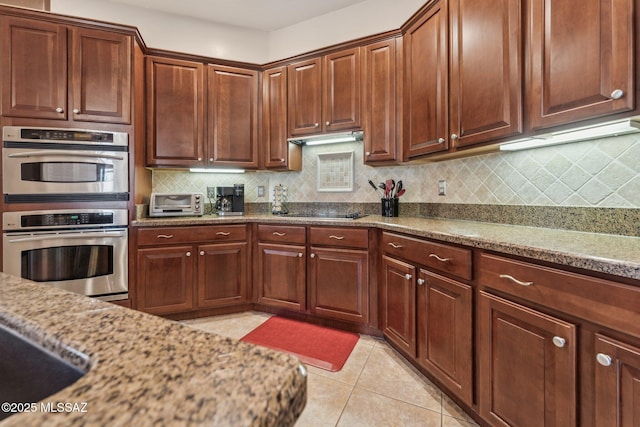 kitchen with tasteful backsplash, double oven, light tile patterned flooring, and light stone countertops