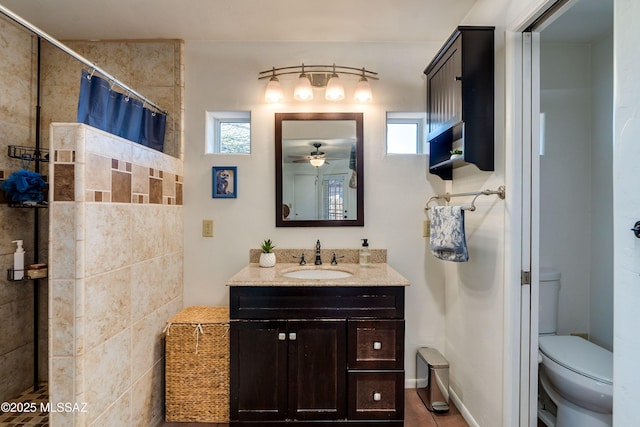 bathroom featuring toilet, tiled shower, vanity, and a ceiling fan