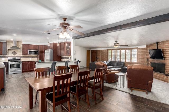 dining area with dark wood-type flooring, a brick fireplace, a ceiling fan, and a textured ceiling