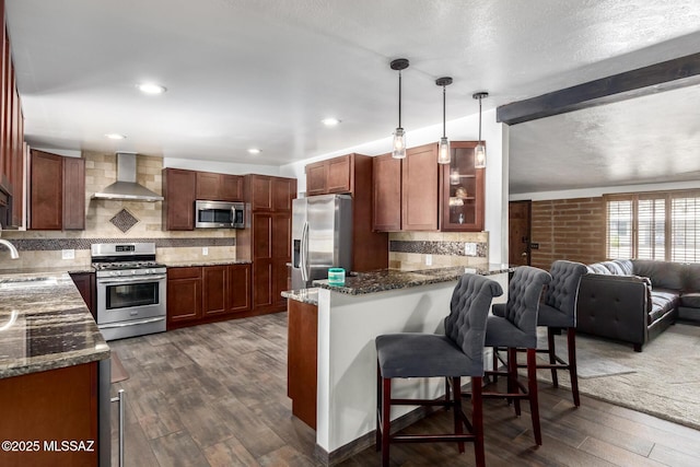 kitchen featuring dark wood-type flooring, a sink, stainless steel appliances, a peninsula, and wall chimney exhaust hood