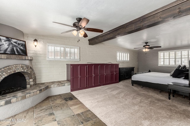 bedroom featuring a ceiling fan, carpet floors, lofted ceiling with beams, a fireplace with raised hearth, and a textured ceiling