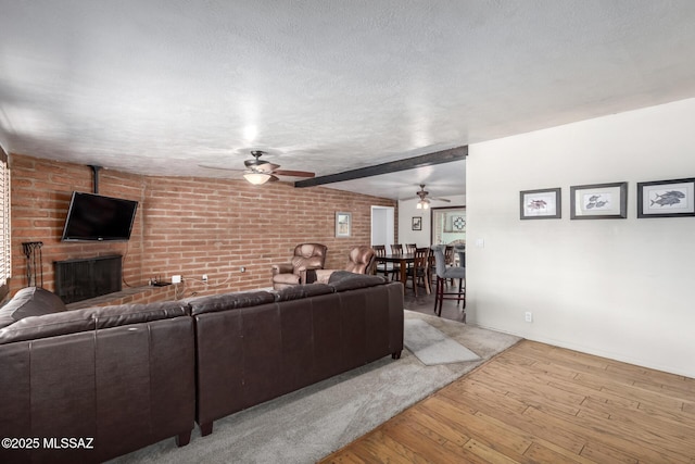 living room with hardwood / wood-style flooring, lofted ceiling with beams, a textured ceiling, brick wall, and a brick fireplace