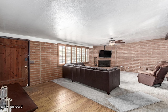 living room featuring a ceiling fan, hardwood / wood-style flooring, a textured ceiling, brick wall, and a fireplace