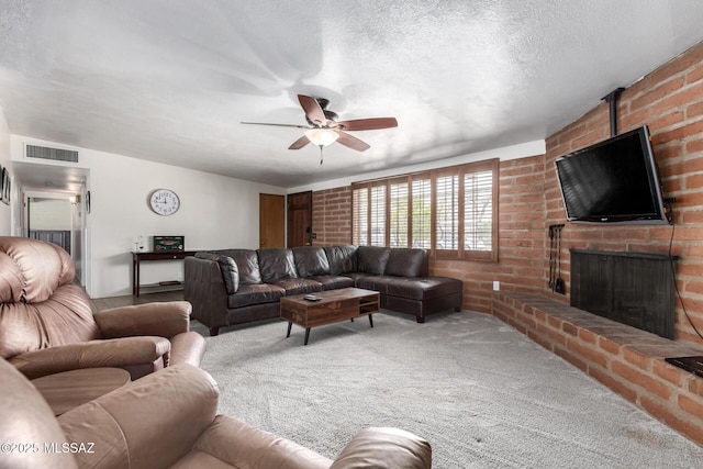 carpeted living area featuring a brick fireplace, a ceiling fan, visible vents, and a textured ceiling