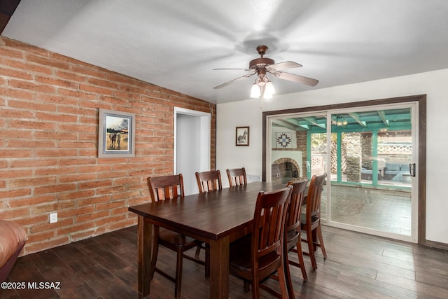 dining area featuring brick wall, a fireplace, dark wood-type flooring, and a ceiling fan