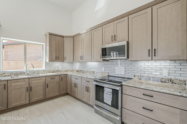 kitchen with light stone counters, decorative backsplash, appliances with stainless steel finishes, and a high ceiling