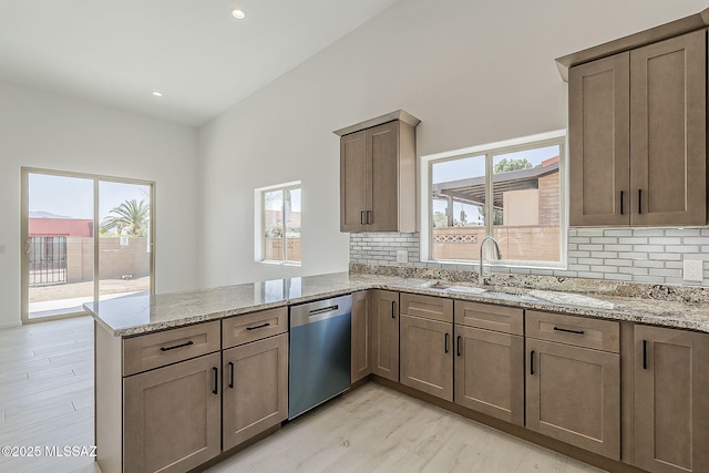 kitchen with backsplash, light stone counters, a peninsula, stainless steel dishwasher, and a sink